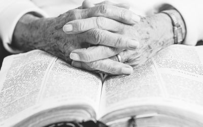 Older person's hands folded on a Bible to illustrate the Legacy of Older Christians